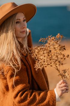 A woman walking along the coast near the sea. An elegant lady in a brown coat and a hat with fashionable makeup walks on the seashore.