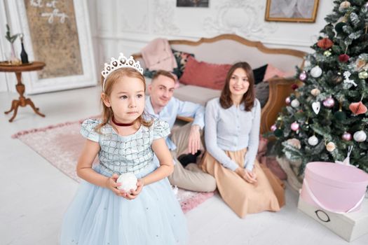 Loving family Mom and dad, little daughter . Parents and baby child having fun near Christmas tree and white fireplace indoors. Merry Christmas and Happy New Year. Cheerful pretty people