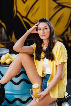 a girl in a yellow shirt with lemon juice in her hands in a city cafe on the street. Portrait of a woman in yellow.