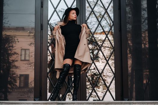 Stylish young woman in a beige coat in a black hat on a city street. Women's street fashion. Autumn clothing.Urban style.