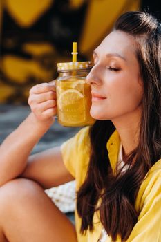 a girl in a yellow shirt with lemon juice in her hands in a city cafe on the street. Portrait of a woman in yellow.