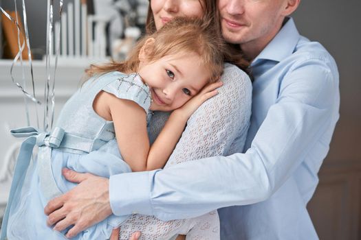 Loving family. Mom and dad hugging little daughter . Parents and baby child having fun near Christmas tree and white fireplace indoors. Merry Christmas and Happy New Year. Cheerful pretty people