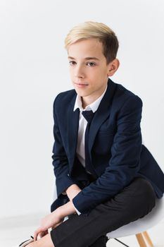 Portrait of stylish school boy teenager in white shirt and jacket against white background with copy space