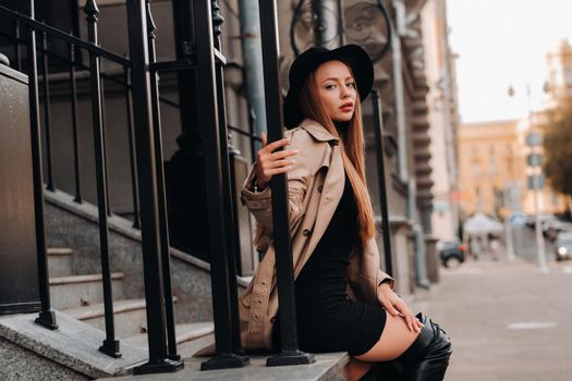 Stylish young woman in a beige coat in a black hat on a city street. Women's street fashion. Autumn clothing.Urban style.