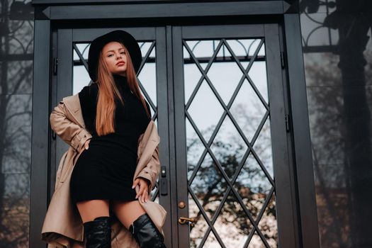 Stylish young woman in a beige coat in a black hat on a city street. Women's street fashion. Autumn clothing.Urban style.