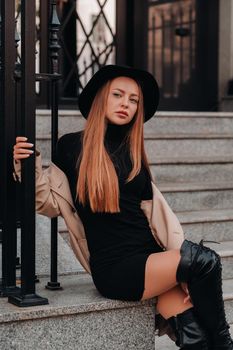 Stylish young woman in a beige coat in a black hat on a city street. Women's street fashion. Autumn clothing.Urban style.