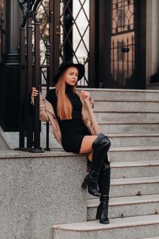 Stylish young woman in a beige coat in a black hat on a city street. Women's street fashion. Autumn clothing.Urban style.