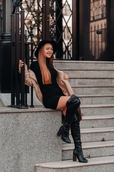 Stylish young woman in a beige coat in a black hat on a city street. Women's street fashion. Autumn clothing.Urban style.