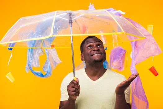 World Environment Day, plastic recycling problem and environmental disaster concept - Surprised african american man looking on trash on yellow.