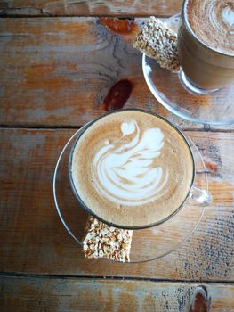 Coffee in glass cup with cookies on wooden table in cafe with lighting background