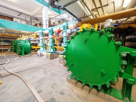 Green water tank. Big heat exchanger in an industrial cellar. Lots of pipes and pumps.