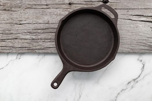 Empty old cast iron skillet set up on white marble  background with flat lay and copy space.