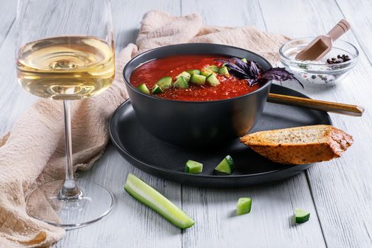 A close-up of a bowl of Spanish traditional cold tomato and cucumber gazpacho soup and a glass of white wine with cereal bread. Summer food. Healthy and vegetarian food. Selective focus.