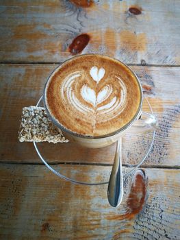 Coffee in glass cup with cookies on wooden table in cafe with lighting background