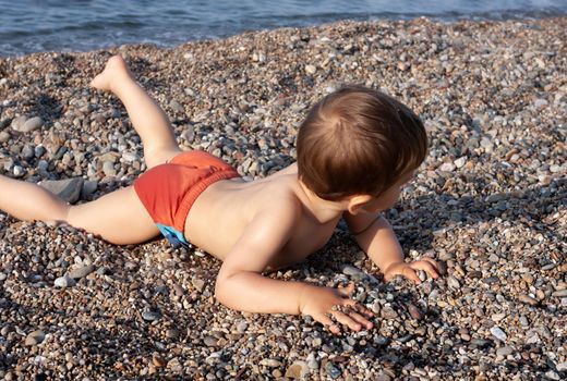 Healthy lifestyle. Little boy resting lying on the stones on the rocky beach on the Mediterranean sea