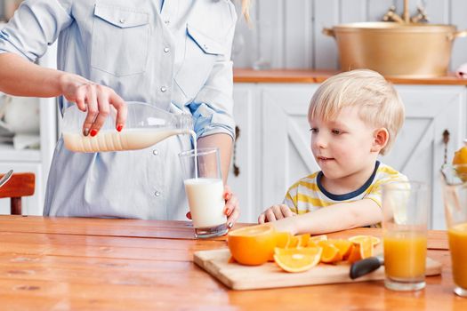 Mother and son are smiling while having a breakfast in kitchen. Mom is pouring milk into glass