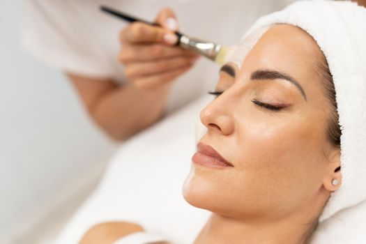 Aesthetics applying a mask to the face of a Middle-aged woman in modern wellness center. Beauty and Aesthetic concepts.