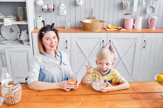 Mother and son are smiling while having a breakfast in kitchen. Bright morning in the kitchen. Healthy Breakfast cereals and fresh fruit