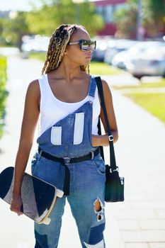 Black girl with sunglasses and skateboard in an urban background.