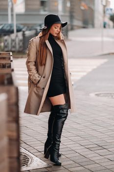 Stylish young woman in a beige coat in a black hat on a city street. Women's street fashion. Autumn clothing.Urban style.