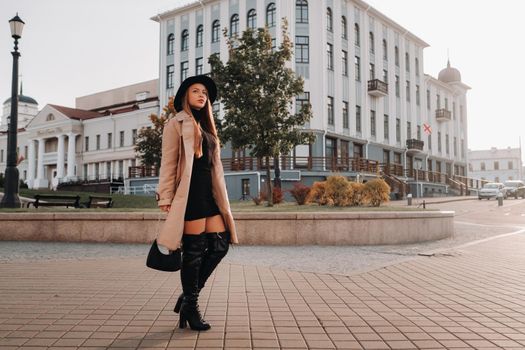 Stylish young woman in a beige coat in a black hat on a city street. Women's street fashion. Autumn clothing.Urban style.