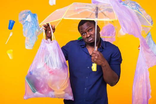 Problem of trash, plastic recycling, pollution and environmental concept - confused man carrying garbage bag on yellow background.