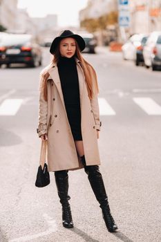 Stylish young woman in a beige coat in a black hat on a city street. Women's street fashion. Autumn clothing.Urban style.