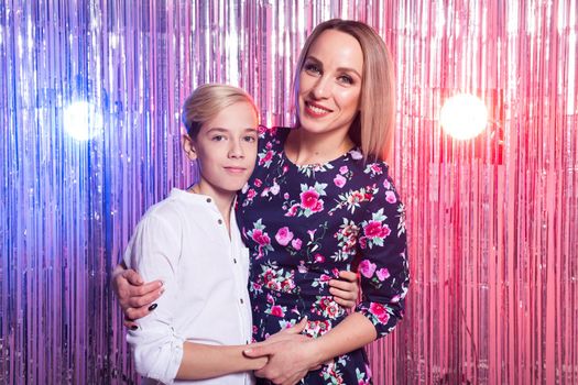 Mothers day, children and family concept - teen boy and his mom embracing on shiny party background