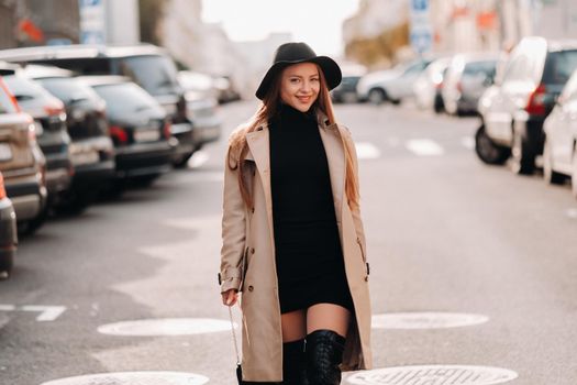 Stylish young woman in a beige coat in a black hat on a city street. Women's street fashion. Autumn clothing.Urban style.