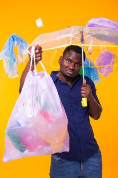Problem of trash, plastic recycling, pollution and environmental concept - confused man carrying garbage bag on yellow background.