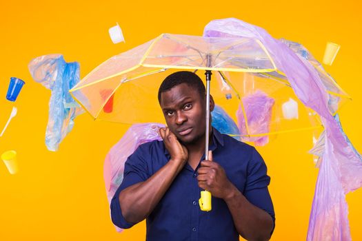 Problem of trash, plastic recycling, pollution and environmental concept - pensive african american man on yellow background with garbage