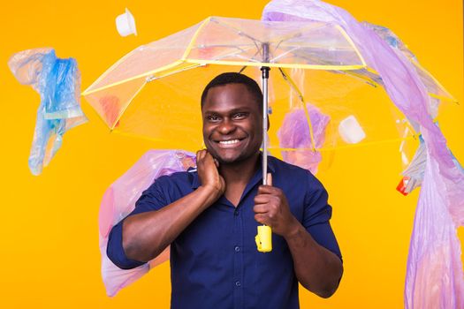 Problem of trash, plastic recycling, pollution and environmental concept - funny african american man carrying garbage for recycling on yellow