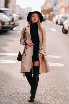 Stylish young woman in a beige coat in a black hat on a city street. Women's street fashion. Autumn clothing.Urban style.