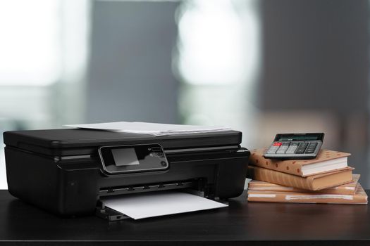 Stack of books and home printer against blurred background, close up