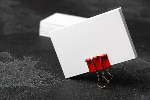 White businesscards united with a paper clip on a black rough background, copy space