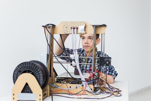 Education, children, technology concept - teen boy is printing on 3d printer