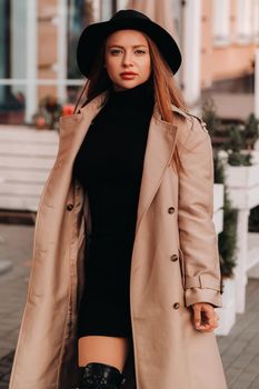 Stylish young woman in a beige coat in a black hat on a city street. Women's street fashion. Autumn clothing.Urban style.