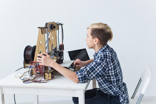 Education, children, technology concept - teen boy is printing on 3d printer