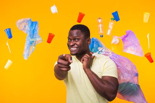 Problem of trash, plastic recycling, pollution and environmental concept - funny african american man carrying garbage for recycling on yellow