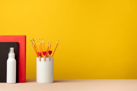 Cup of pencils and notepads on desk against yellow background, front view