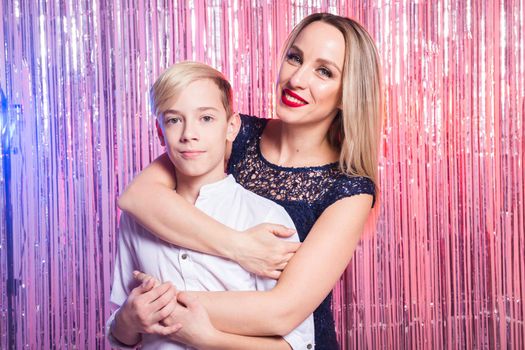 Mothers day, children and family concept - teen boy and his mom embracing on shiny party background