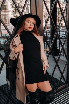 Stylish young woman in a beige coat in a black hat on a city street. Women's street fashion. Autumn clothing.Urban style.