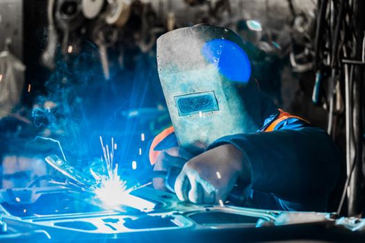 Welder man in a protective mask of iron is engaged in the process of welding and metal work in the workshop of an industrial plant.