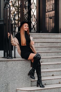 Stylish young woman in a beige coat in a black hat on a city street. Women's street fashion. Autumn clothing.Urban style.