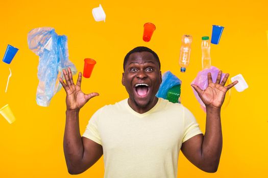 Plastic recycling problem, ecology and environmental disaster concept - Scared man screaming on yellow background with trash. He is worried about ecology disaster.