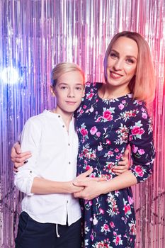 Mothers day, children and family concept - teen boy and his mom embracing on shiny party background