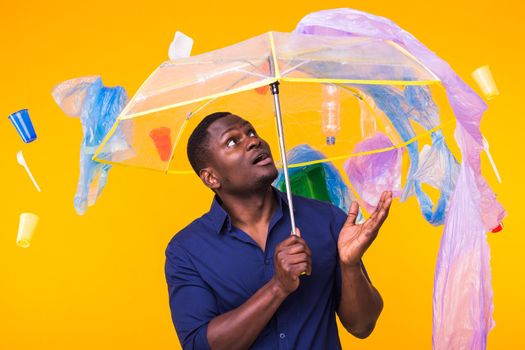 World Environment Day, plastic recycling problem and environmental disaster concept - Surprised african american man looking on trash on yellow.