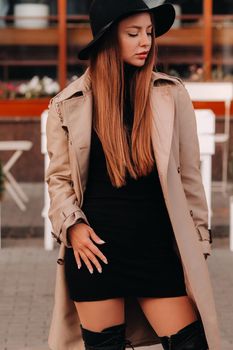 Stylish young woman in a beige coat in a black hat on a city street. Women's street fashion. Autumn clothing.Urban style.