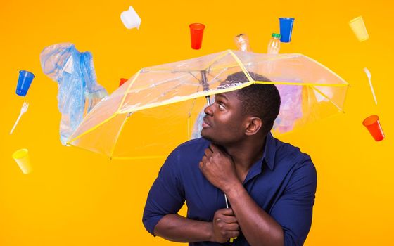 World Environment Day, plastic recycling problem and environmental disaster concept - Surprised african american man looking on trash on yellow.