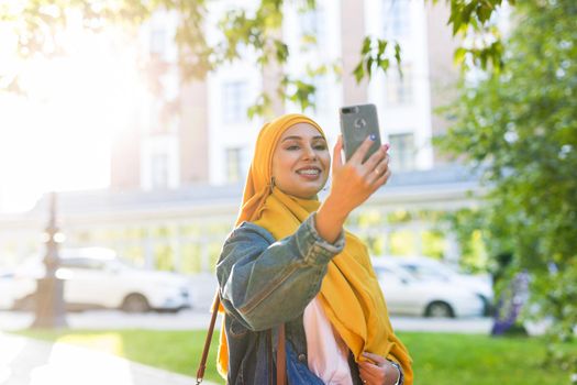 Muslim girl in hijab makes a selfie on the phone standing on the street of the city.
